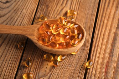 Tahta bir masada tahta kaşıkta balık yağı kapsülleri..