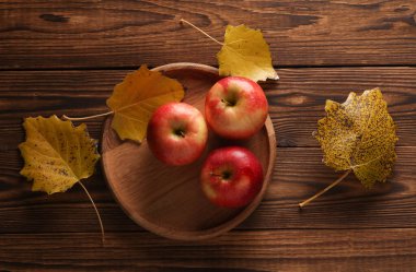 Elma tabağı ve sonbahar yaprakları ahşap bir masada.