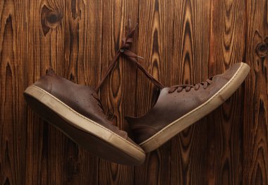 Deri ayakkabılar tahta arka plandaki bağcıklardan sallanıyor.