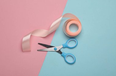 Mavi-pembe pastel arka planda makaslı bir kurdele rulosu.