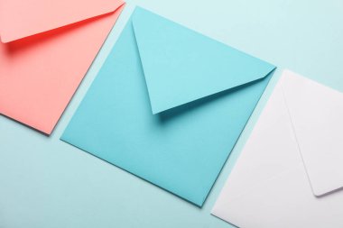 Mavi pastel arka planda pembe, beyaz ve mavi kağıt zarflar.