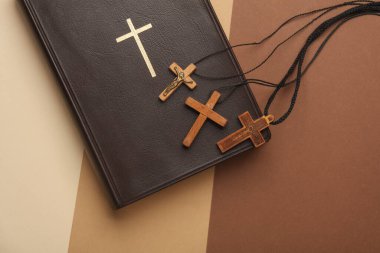 İncil kitabı ve ahşap Hıristiyan haçları bej arka planda. Üst görünüm