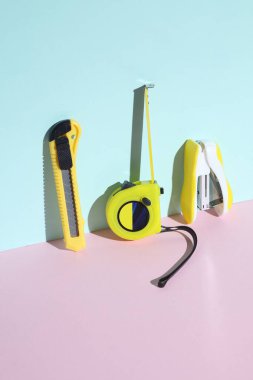 Bant mezurası, zımba ve kırtasiye bıçağı mavi-pembe pastel arka planda.