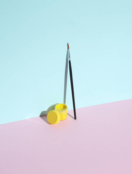 Желтый гуашь краски в банке и кисти на пастельном фоне