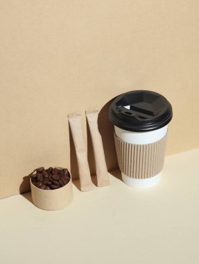 Sıcak içecekler için karton bardak, pakette şeker ve gölgeli bej arkaplanda kahve çekirdeği.