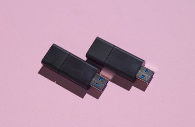 Pembe arka planda iki siyah USB flaş bellek.