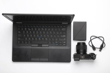 Modern bir fotoğrafçının ekipmanı. Beyaz arka planda dizüstü bilgisayar, kamera ve harici hard disk var. Düz yatıyordu. Üst görünüm