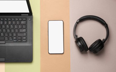 Laptop, akıllı telefon ve renkli pastel arka planda kablosuz kulaklık. Modern insanların hediyeleri. Düz yatıyordu