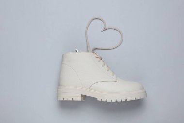 Gri arka planda kalp şeklinde bağcıkları olan beyaz kadın deri çizmesi. Aşk konsepti. Üst görünüm