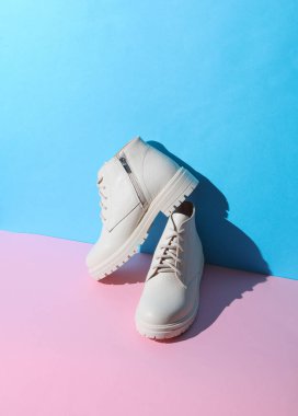 Pembe mavi arka planda, gölgeli beyaz kadın deri çizmeleri. Yaratıcı yerleşim 