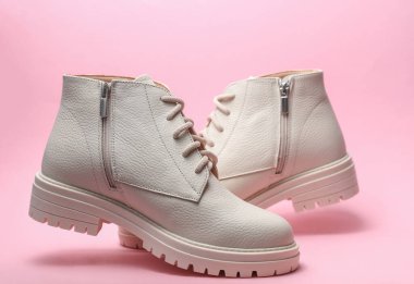 Pembe arka planda yüzen beyaz deri kadın çizmeleri. Minimalizm modadır.