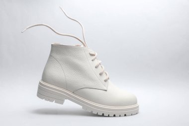 Gri arka planda uçan bağcıklı beyaz deri çizme..