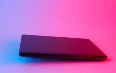 Mavi-pembe neon ışıkta süzülen modern kapalı dizüstü bilgisayar