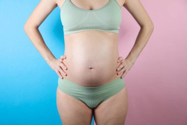 Mavi pembe arka planda iç çamaşırlı hamile bir kadın.