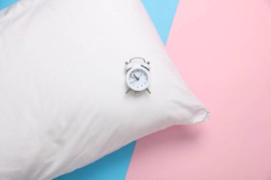 Mavi-pembe pastel arka planında alarm olan beyaz yastık. Uyku vakti. Üst görünüm