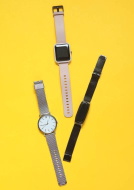 Sarı arka planda modern akıllı ve analog saatler ve bilezik. Üst görünüm