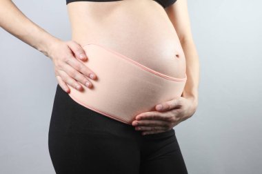 Sırtı ve göbeği için ortopedik kemeri olan hamile bir kadın. Hamile kadınlar için bandaj. Üçüncü üç aylık dönem için özel kemer. Gri bir arkaplanda stüdyo çekimi