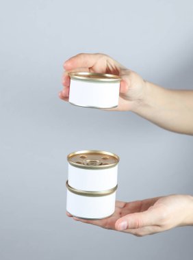 Beyaz etiketli teneke kutu konserve yiyecekler. Gri bir stüdyonun arka planında bir kadın elinde tasarımın için maket.