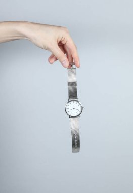 Gri stüdyo arka planında analog kol saati tutan kadın.
