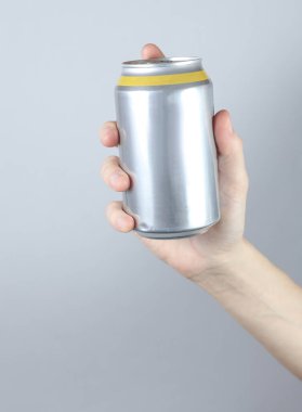 Bira, soda ya da enerji içeceği için gri stüdyo arka planında alüminyum kutu tutuyordu..