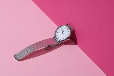 Pembe pastel arka planda gölgeli kadın analog gümüş kol saati. Yaratıcı düzen. Minimalizm
