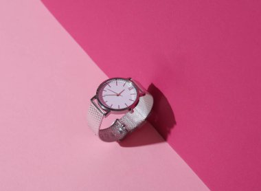 Pembe pastel arka planda gölgeli kadın analog gümüş kol saati. Yaratıcı düzen. Minimalizm