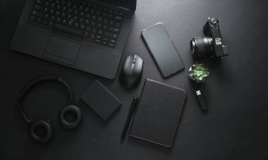 Modern cihazlar ve siyah aksesuarlar. Laptop, kamera, akıllı telefon, stereo kulaklıklar, not defteri, harici sabit disk, siyah arka planda USB flash disk. Çalışma alanı. Düz yatıyordu. Üst görünüm