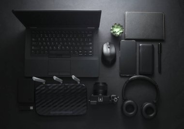 Modern siyah aletler ve aksesuarlar. Laptop, kamera, akıllı telefon, stereo kulaklıklar, not defteri, harici sabit disk, siyah arka planda USB flash disk. Fotoğrafçı çalışma alanı. Düz yatıyordu. Üst görünüm