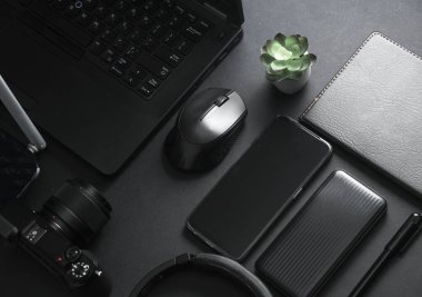 Modern siyah aletler ve aksesuarlar. Laptop, kamera, akıllı telefon, stereo kulaklıklar, not defteri, harici sabit disk, siyah arka planda USB flash disk. Fotoğrafçı çalışma alanı. Düz yatıyordu. Üst görünüm