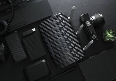 Modern siyah cihazlar ve aksesuarlar, laptop, kamera, akıllı telefon, harici sabit disk, kablosuz ağ yönlendirici, USB flash disk, siyah arka planda güç bankası. Fotoğrafçı ekipmanı. Çalışma alanı. Düz yatıyordu. Üst görünüm
