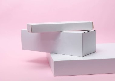 Pembe arka plandaki sunum ürünleri için farklı şekillerde beyaz karton kutular. Tasarım için model.