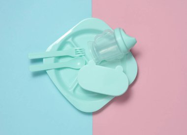 Mavi-pembe arka planda bebeği beslemek için plastik tabak seti. Üst görünüm