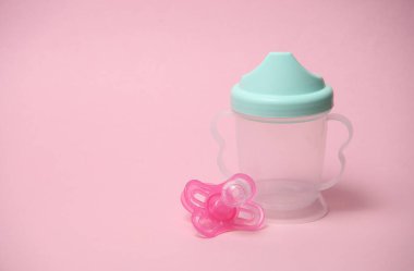 Pembe arka planda bebek için içki kasesi ve bebek emziği.