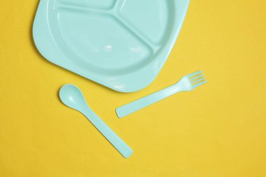 Sarı arka planda bebeği beslemek için kaşık ve çatalla ayrı plastik tabak. Üst görünüm
