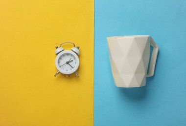 Mavi-sarı arka planda alarm saati olan beyaz geometrik bardak. İş konsepti