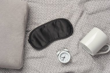 Battaniyenin üzerinde bir fincan ve çalar saatle uyuyan maske. Üst görünüm