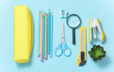 Kırtasiyeli sarı kalem çantası ve mavi arka planda okul aksesuarları. Okul konseptine geri dönelim. Üst Manzara. Düz yatıyordu