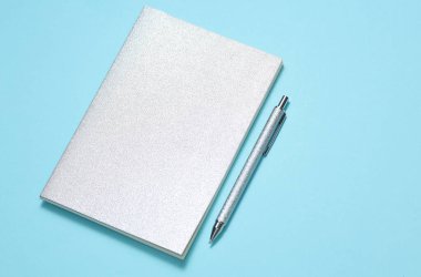 Mavi arka planda gümüş kapaklı ve kalemli not defteri