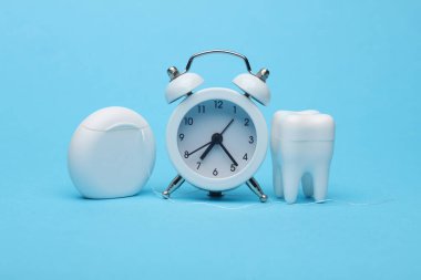 Ağız boşluğunla ilgilenme zamanı. Diş modelli çalar saat ve mavi arka planda diş ipi.