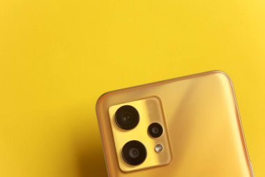 Sarı arka plandaki modern akıllı telefonun üç kamerası.