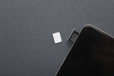 Gri arka planda SIM kartı olan akıllı telefon ve tepsi. Düz yatıyordu