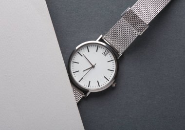 Gri arka planda metal veya gümüş kayışlı kadın bileği analog saati. Düz yatıyordu. Üst görünüm