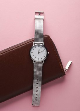 Pembe arka planda cüzdanı olan kol saati.