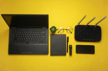 Not defterli dizüstü bilgisayar, akıllı telefon, kablosuz ağ yönlendirici ve sarı arka planda ofis malzemeleri. Çalışma alanı. Üst Manzara. Düz yatıyordu