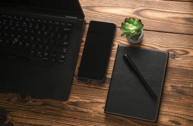 Akıllı telefonlu dizüstü bilgisayar ve tahta arka planda not defteri.