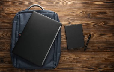 Çalışmak ve çalışmak için modern aletler. Sırt çantası, dizüstü bilgisayar ve tahta arka planda defter. Üst görünüm