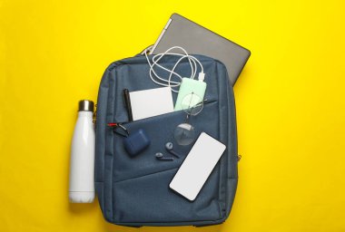 İş için modern cihazlar ve aksesuarlar sarı arka planda sırt çantasında. Üst Manzara. Düz yatıyordu