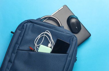 Mavi arka plandaki sırt çantasında çalışmak ve çalışmak için modern cihazları ve aksesuarları olan bir laptop. Üst Manzara. Düz yatıyordu