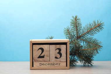 23 Aralık tarihli ahşap blok takvimi ve masa ve mavi zemin üzerinde çam ağacı