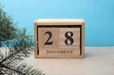 28 Aralık tarihli tahta blok takvimi ve masa ve mavi arkaplanda çam ağacı